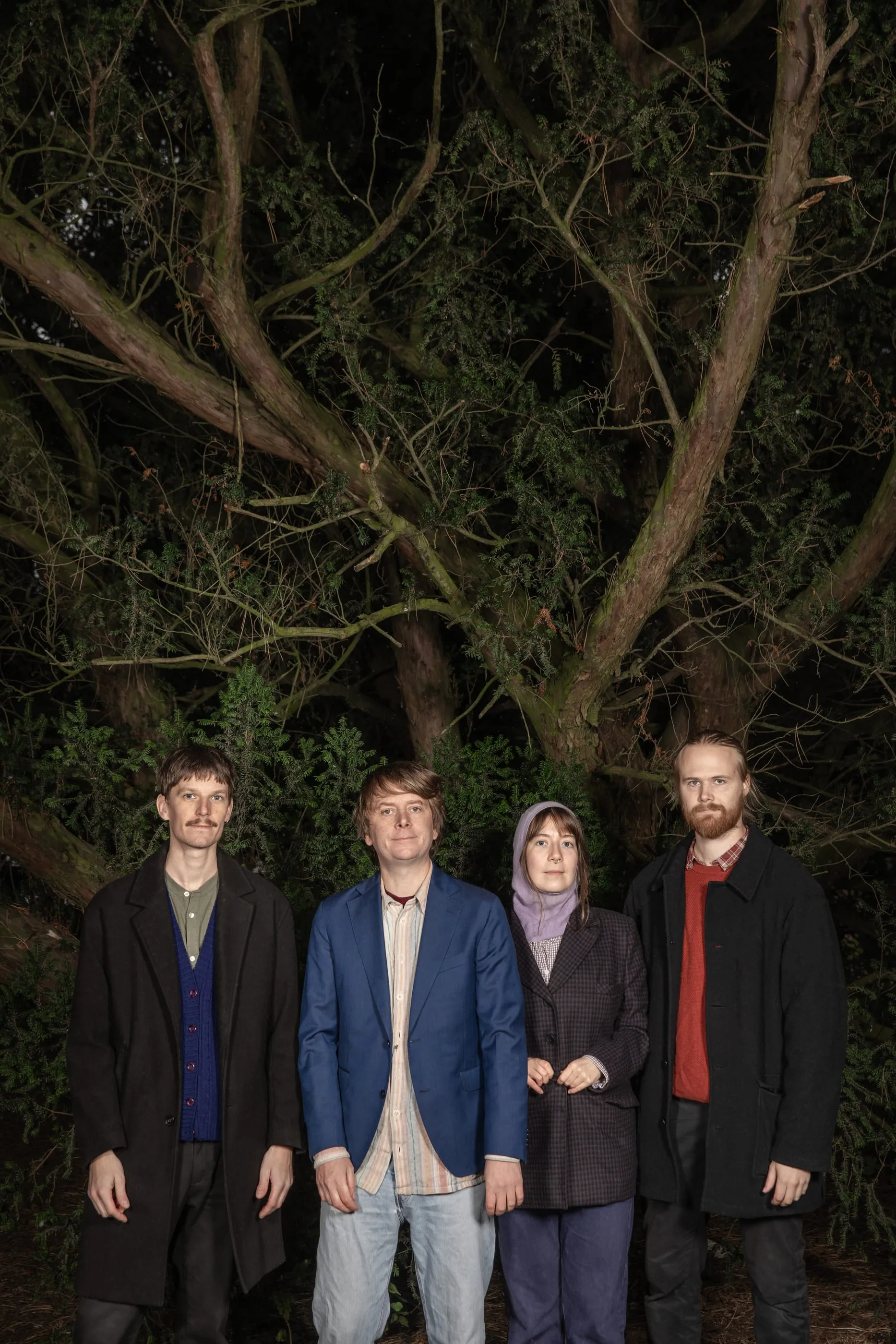 The band in coats under a large tree in the evening.